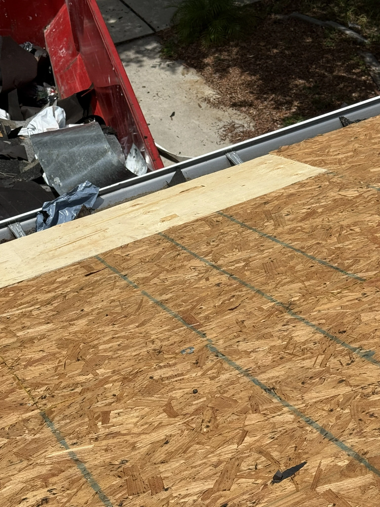 new plywood decking strip installed at the roof eave above a dumpster of tear-off debris