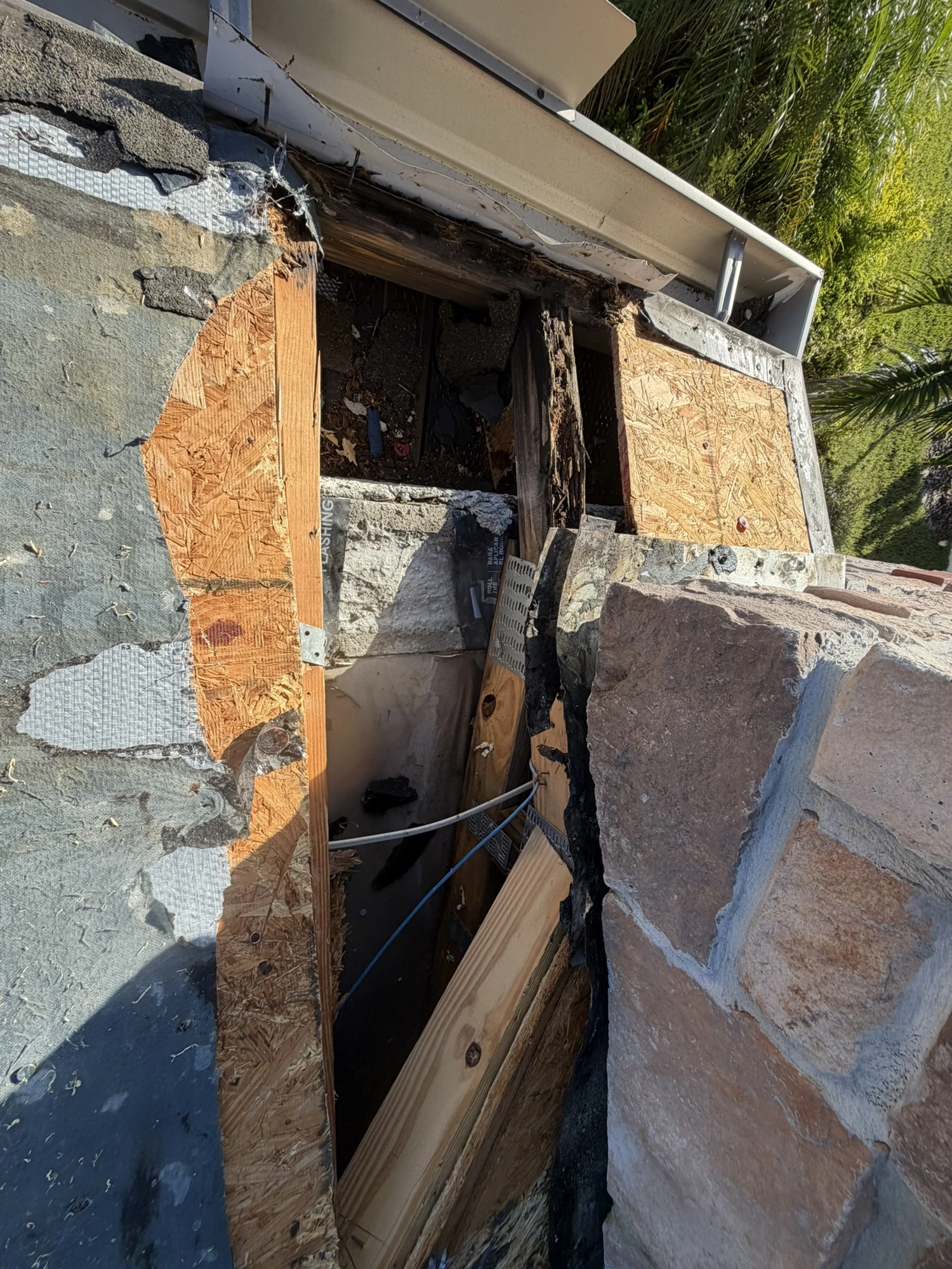 rotted roof decking exposed beside a stone chimney during a Riverview roof leak repair