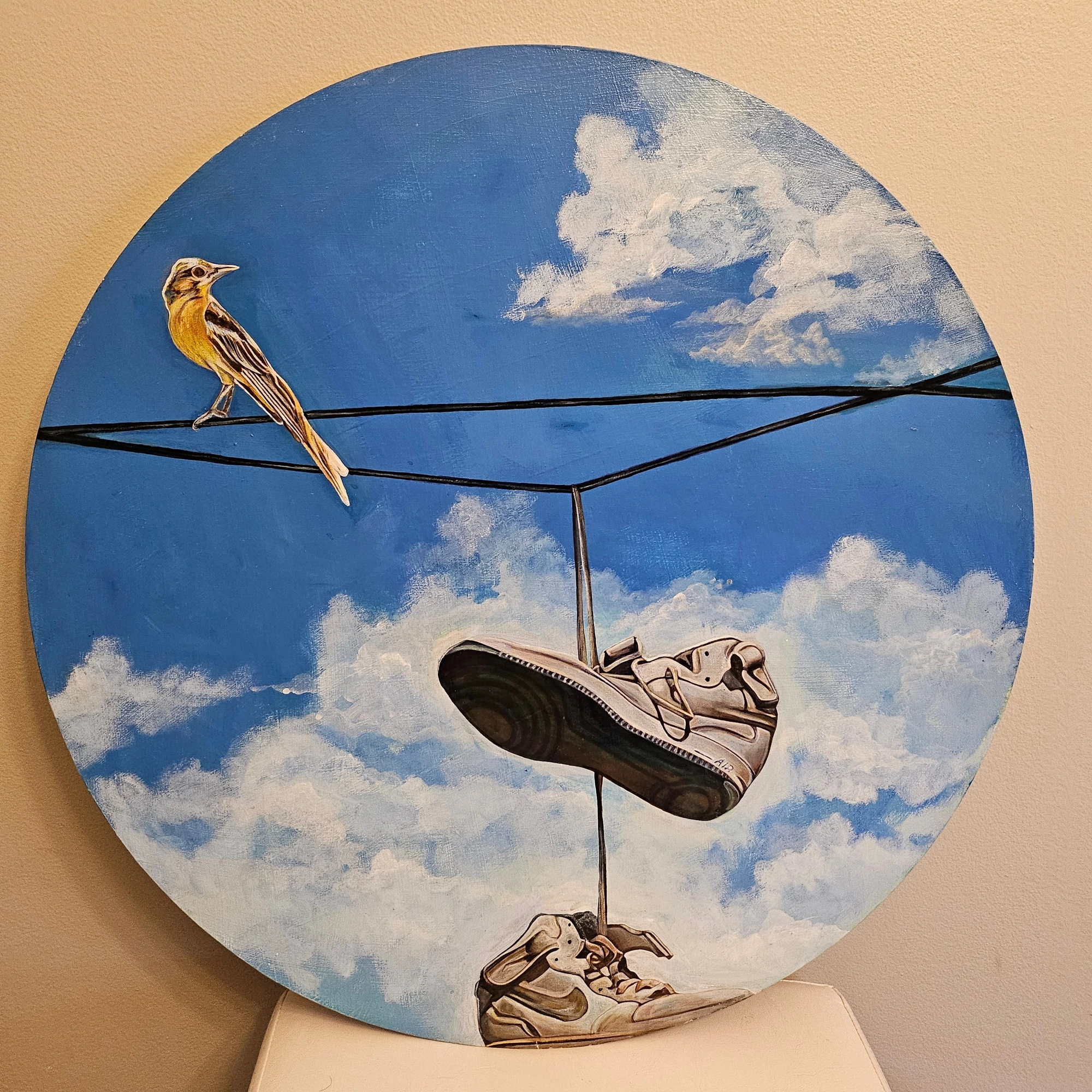 Circular artwork of a bird on a wire with shoes hanging below