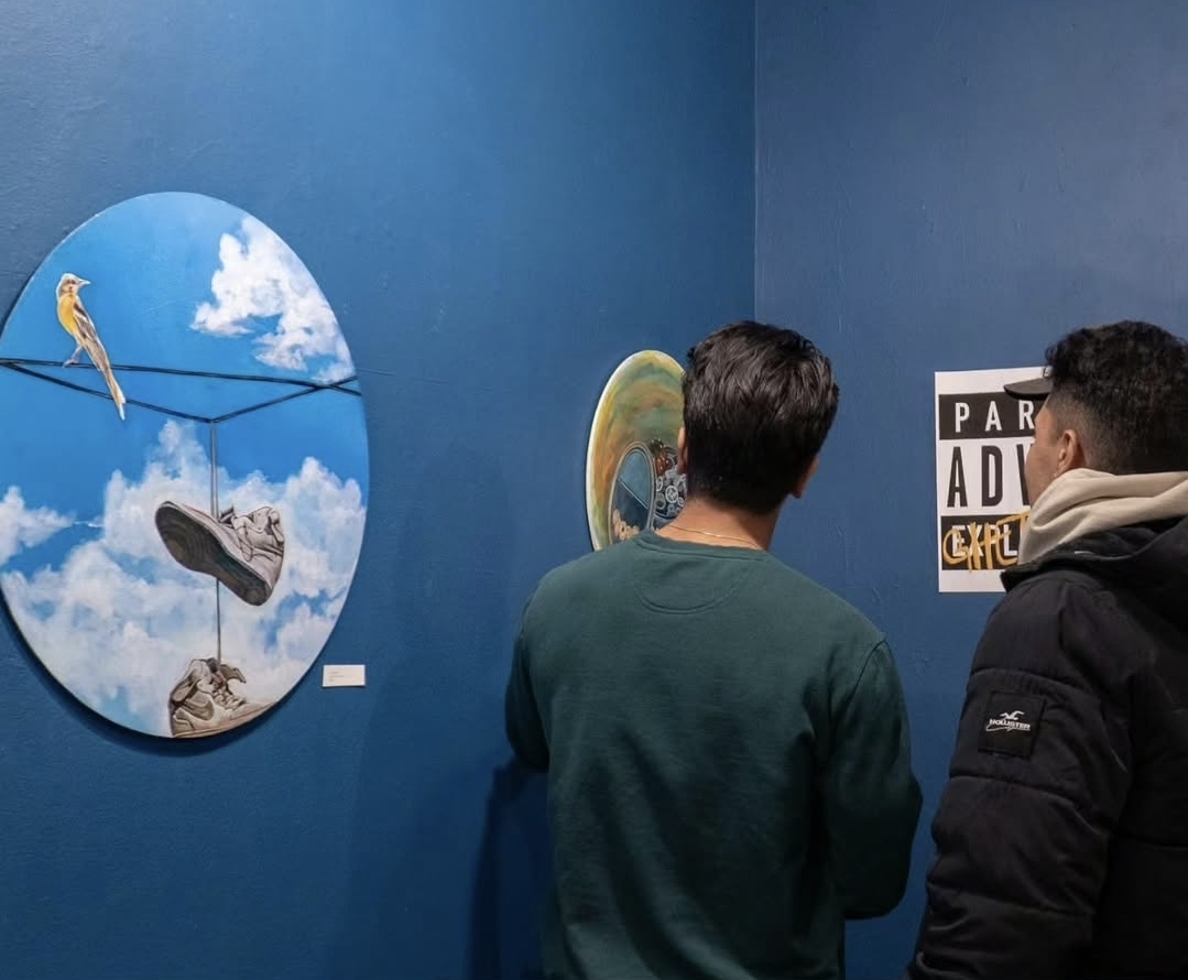 Landscape installation view of visitors and artworks on a bright blue gallery wall