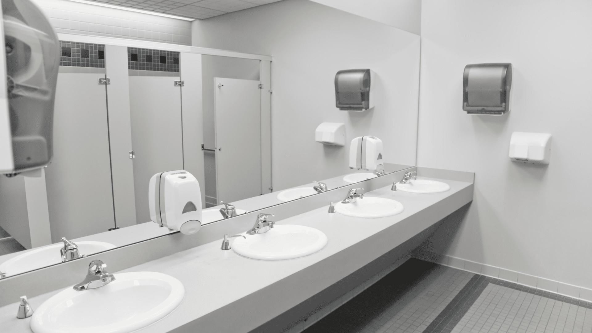 Clean commercial restroom with row of sinks, mirrors, and stainless paper towel dispensers