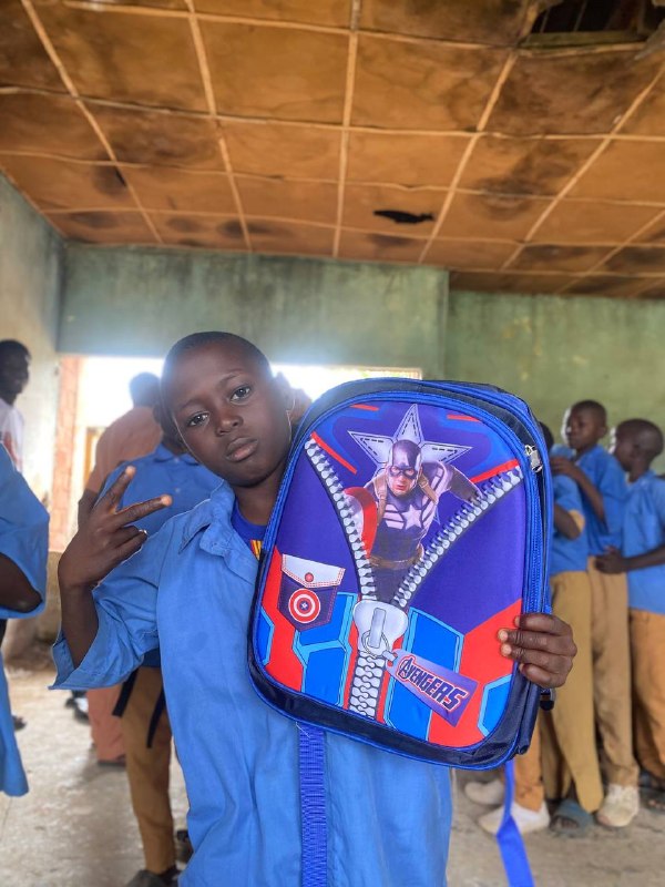 A student proudly holds up his new backpack in class
