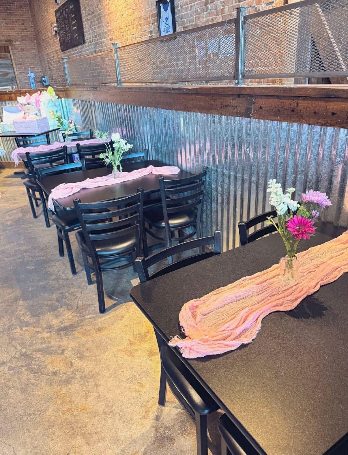 Event hall with long dark tables, blush table runners and fresh flowers beneath exposed brick