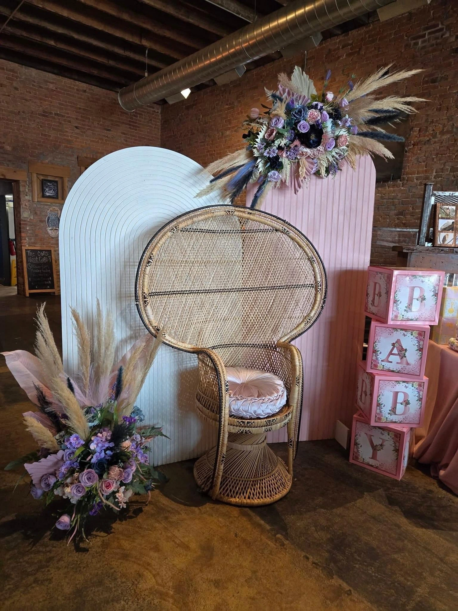 Wicker peacock chair with pampas and floral arrangements beside baby shower blocks