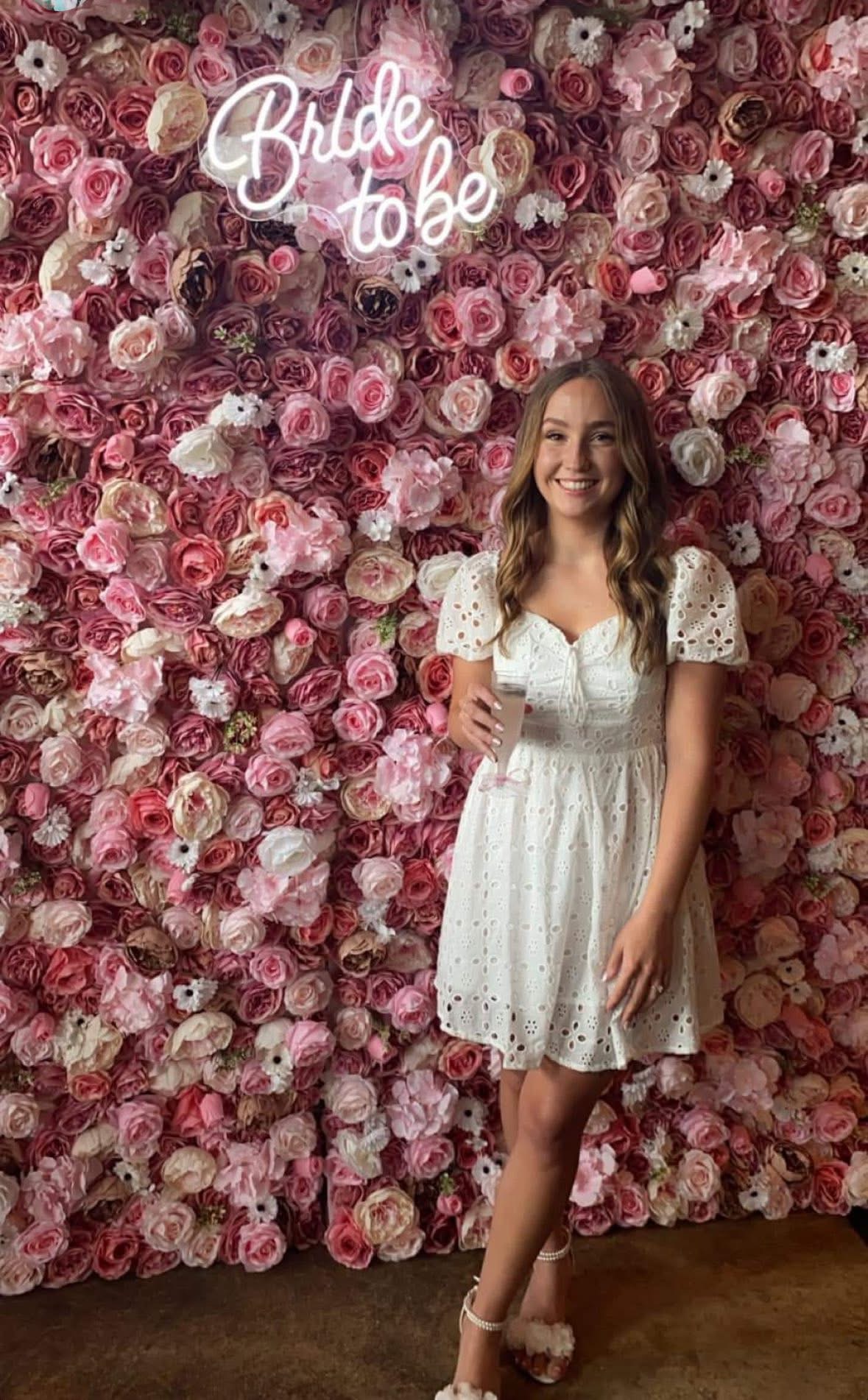 Bride-to-be posing before a pink flower wall with a neon sign