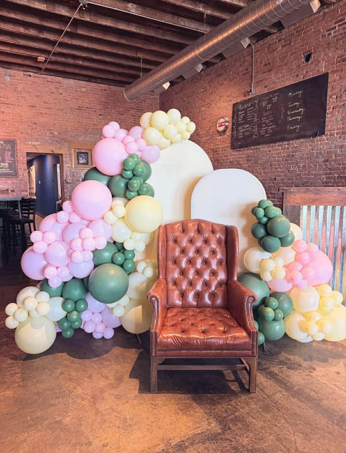 Leather chair with pink, green and yellow balloon garlands beneath timber beams