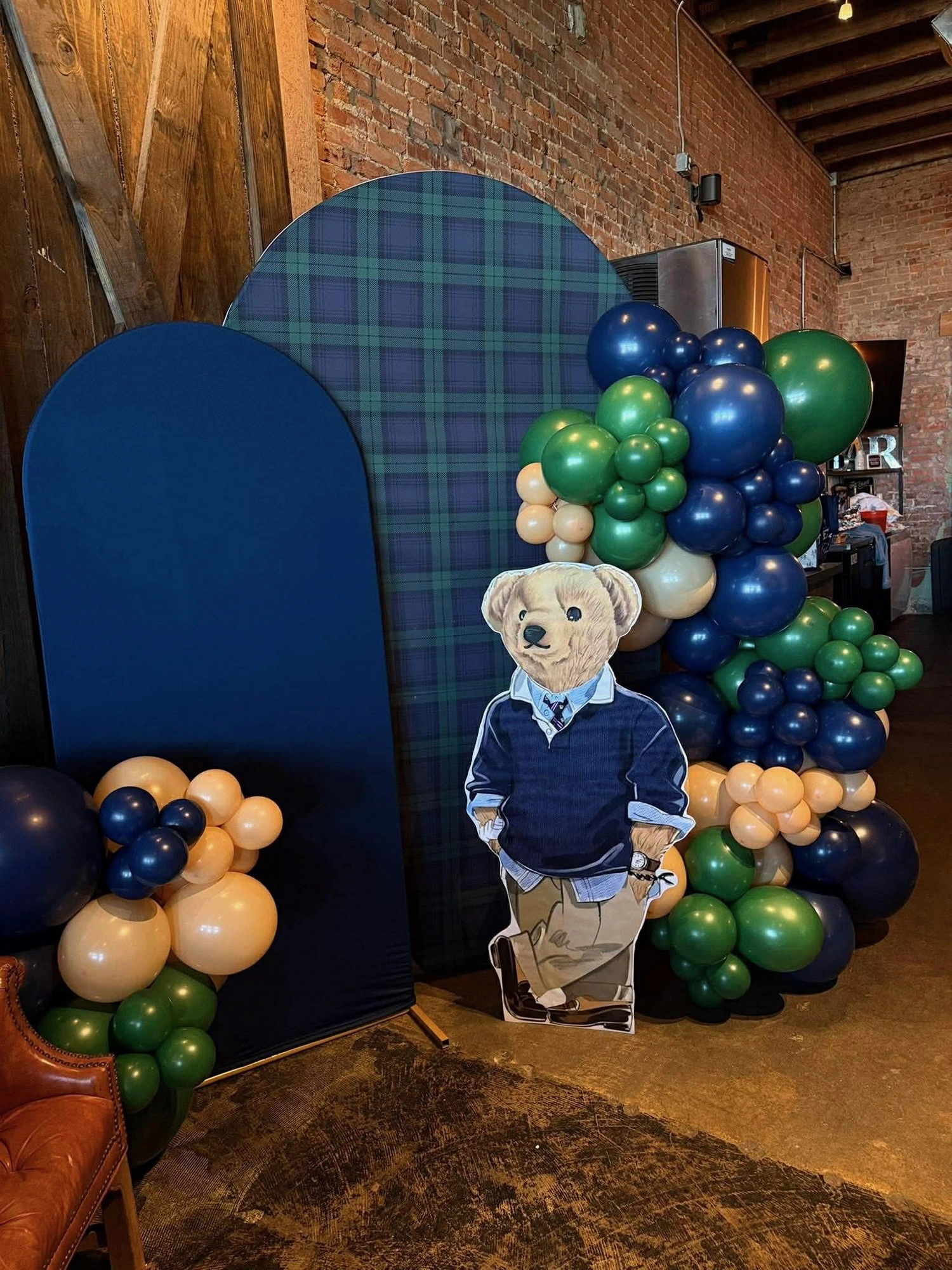 Baby shower photo backdrop with navy and green balloon garland and a teddy bear cutout