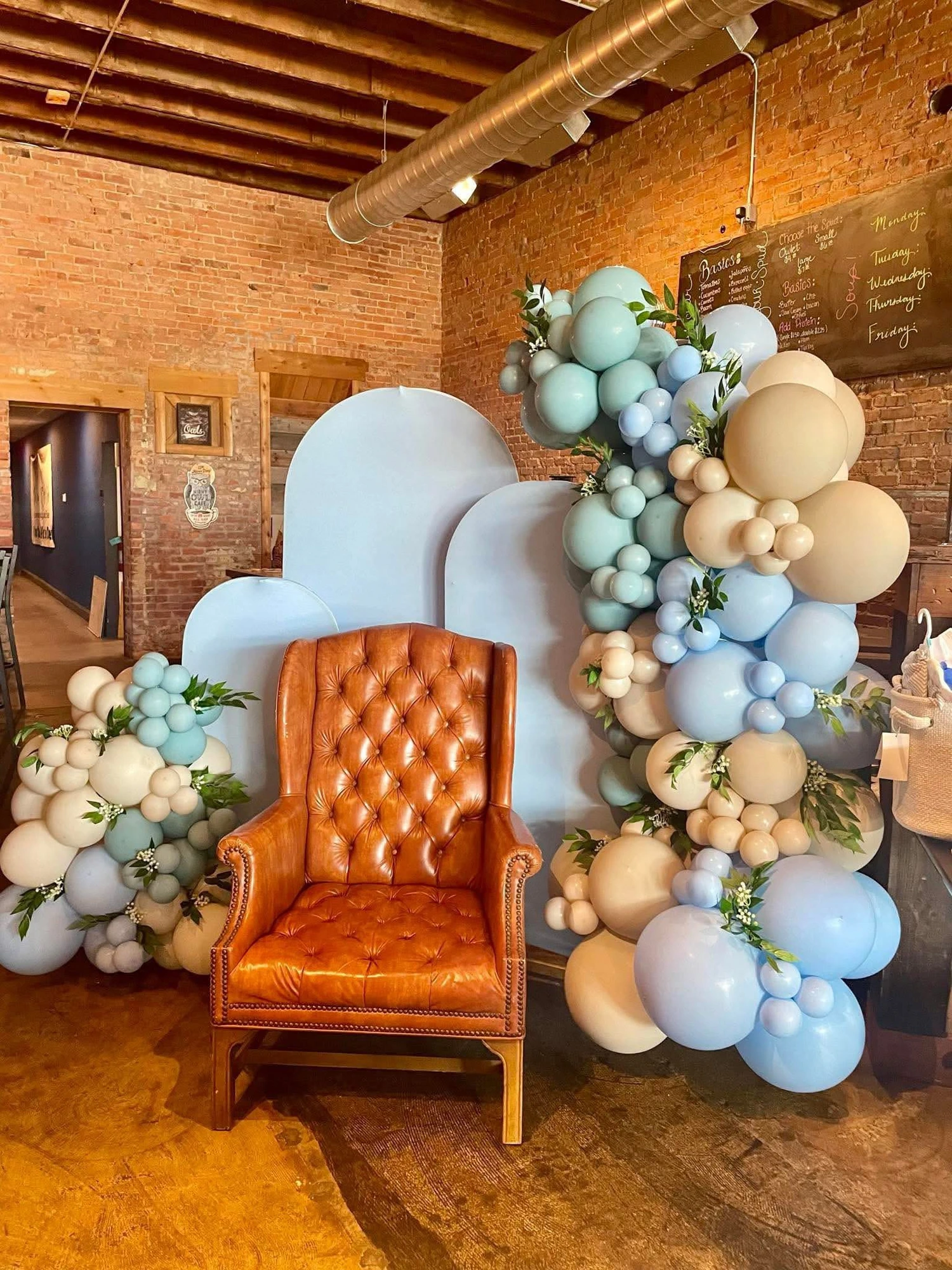 Tufted leather chair framed by a blue and cream balloon garland against exposed brick